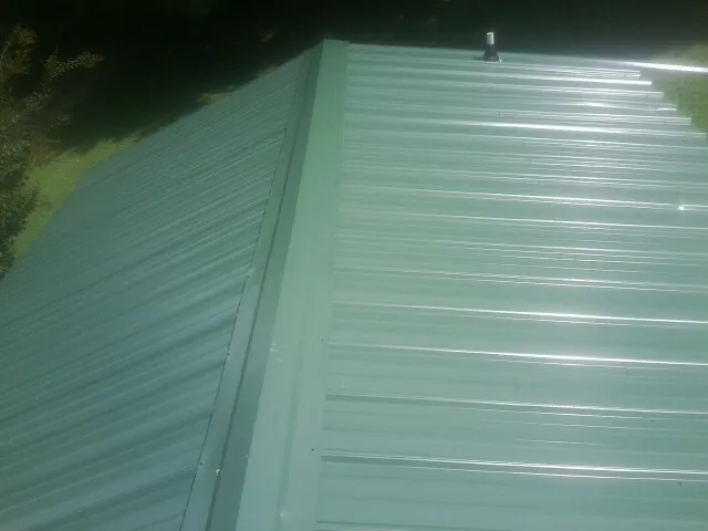 New green metal panels meeting at the ridge of a roof — Flat Roof Repair work by our crew in Paducah