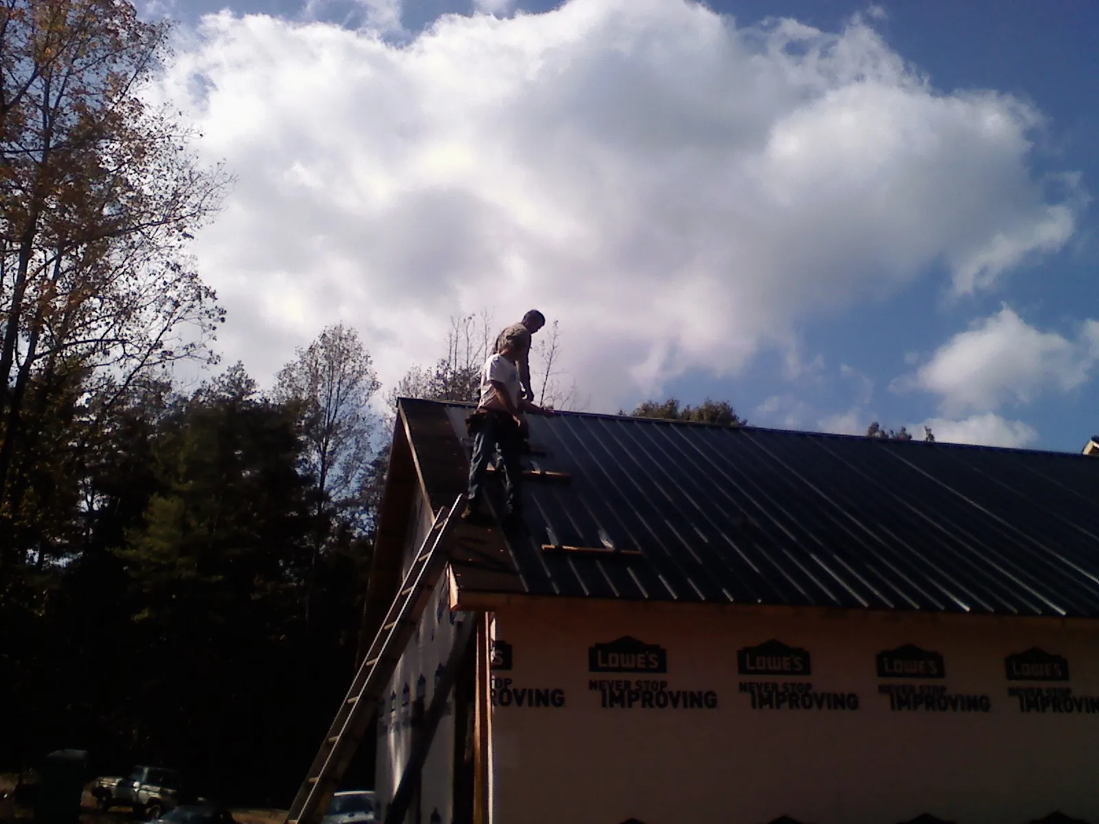 Roofer fastening dark metal panels high against a cloudy sky, from a Roof Inspection job in Paducah