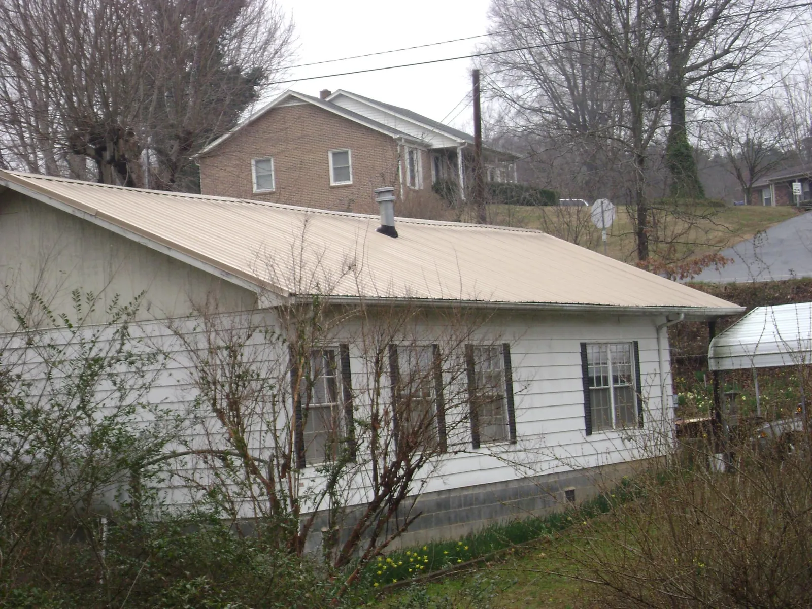 Tan metal roof on a white sided house set into a hillside — Commercial Roofing by Roofing Brothers in Paducah